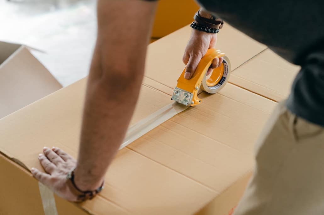 A man sealing a cardboard box with scotch tape.