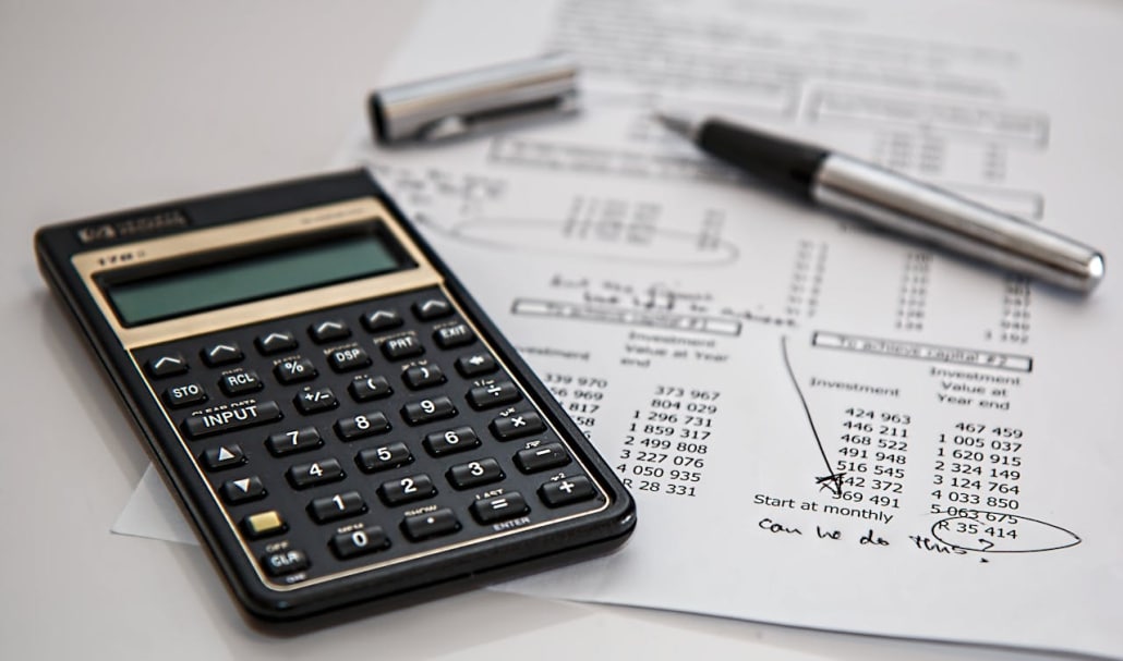 Calculator, piece of paper, and a pen on a white surface.